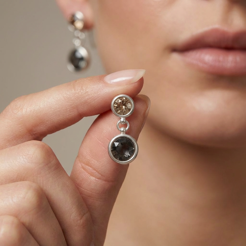 Close-up of a woman holding a pair of silver earrings with gemstones.